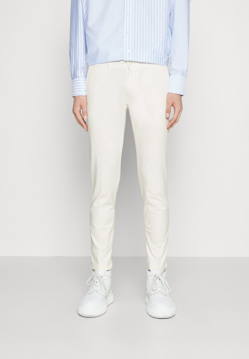 Białe, wąskie spodnie z gładkiego materiału; do tego jasnoniebieska koszula w paski na guziki oraz białe tenisówki.