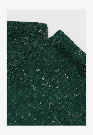 Groene gebreide stof met glanzende metalen draden die er doorheen zijn geweven, gevouwen aan de randen op een lichte achtergrond.