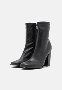 Bottines noires en cuir lisse avec un haut talon bloc, dotées d'une fermeture éclair à l'avant et d'un design à bout pointu.