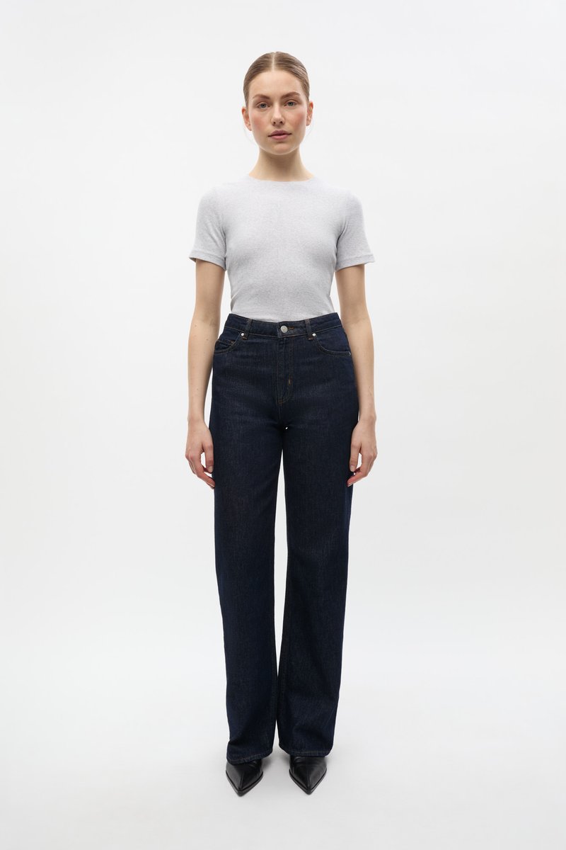 Graues kurzärmliges T-Shirt, kombiniert mit hochgeschnittenen dunkelblauen Jeans. Die Jeans haben einen geraden Schnitt und ein klassisches Fünf-Taschen-Design.