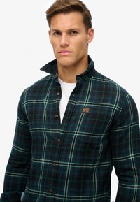 Karo flanellen shirt in donkergroen en zwart met een wit ruitpatroon. Voorzien van een button-down kraag en een logo patch op de borstzak.