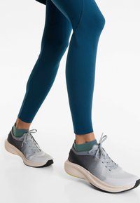 Teal leggings and gray running shoes with mesh and rubber accents. Shoes feature a cushioned sole and flat laces, complemented by green socks.