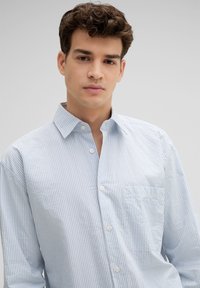 Hellblau und weiß gestreifte Button-Down-Hemd mit Kragen, langen Ärmeln und einer Brusttasche. Weicher Baumwollstoff mit lockerem Schnitt.