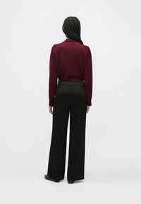 Top maro închis cu mâneci lungi, asortat cu pantaloni negri cu picioare largi, având o textură netedă și un luciu subtil al țesăturii. Vedere doar din spate, fără detalii vizibile.