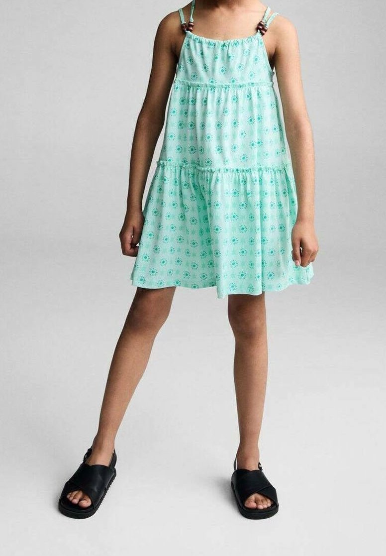 Vestido sin mangas verde menta con estampado floral, diseño de capas y detalles de cuentas en las tiras. Combinado con sandalias planas negras.