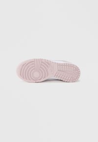 Vaaleanpunainen tennarin pohja, jossa on kuvioidut kumikuviot, sisältäen pyöreitä ja suorakaiteen muotoisia kuvioita pitävyyttä varten. Puhtaan ja minimalistisen tyylin.