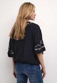 Blusa nera con motivi floreali ricamati sulle maniche e sul collo, caratterizzata da una vestibilità ampia e maniche corte. Abbinata a jeans blu.