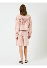 Lyserød denimjakke med frynse detaljer på ryggen, parret med matchende shorts. Outfittet har en afslappet pasform og diskret syninger.