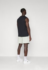 Black sleeveless top, light green shorts, white sneakers, and socks. Simple design with no visible patterns or hardware details. Back view.