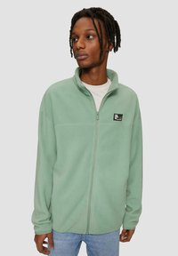 Hellgrüne Fleecejacke mit hohem Kragen, Frontreißverschluss und kleinem schwarzen Logopatch. Weicher Stoff und lässige Passform.