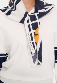 Soft, lightweight sweater in cream with navy stripes. A patterned scarf in navy and white, featuring a yellow accent, is tied at the neck.
