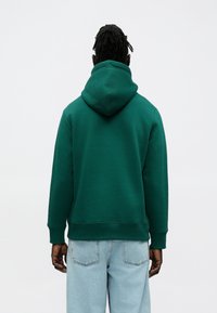 Sudadera con capucha de algodón verde con una capucha espaciosa, puños y dobladillo acanalados, combinada con jeans de mezclilla azul claro. Diseño sencillo, sin patrones visibles.