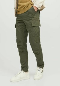Pantaloni cargo verzi cu multiple buzunare, slim fit, confecționați dintr-un material ușor, asortați cu adidași albi și un top stratificat.