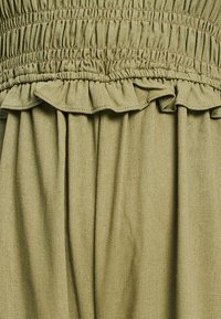Tissu vert olive avec une finition texturée, présentant un design smocké en haut et des accents froncés, créant une apparence superposée.