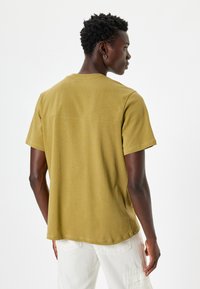 Kortærmet, olivengrøn T-shirt med afslappet pasform, blødt stof og en søm detalje på ryggen. Kombiner med lysere bukser.