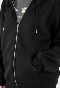 Sweat à capuche zippé noir en tissu mélangé coton, doté d'une poche avant, de poignets côtelés et d'une capuche ajustable avec cordon de serrage.