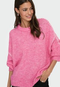 Roze gebreide trui met een chunky textuur, voorzien van een hoge halslijn en zijkanten. Oversized pasvorm met een verlengd schouderdesign.