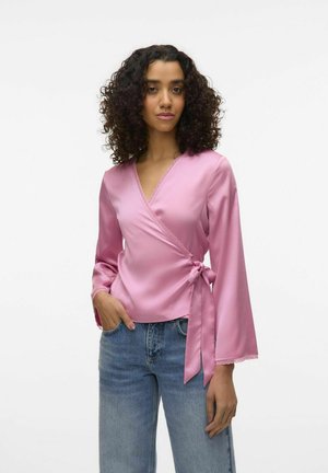 Rosa satinomslagen topp med långa ärmar och spetsdetaljer, knuten vid midjan. Kombineras med ljusblå högmidjade jeans.