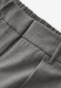 Pantaloni grigi con vita elastica, davanti piatto e una texture sottile. Le pieghe creano un aspetto sartoriale con un design contemporaneo.