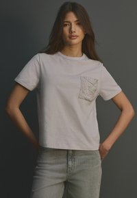Světlé šedé bavlněné tričko s kulatým výstřihem a krátkými rukávy. Obsahuje texturovaný, vyšívaný design kapsy na levém prsu.