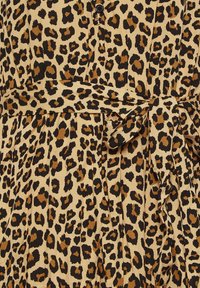 Šaty s leopardím potiskem, které mají béžové pozadí se hnědými a černými skvrnami, zavázaný pas a detailování knoflíky. Měkká tkanina s záhyby.