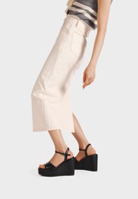 Sandali neri a zeppa con cinturino alla caviglia e tomaia in pelle liscia, abbinati a una gonna in denim beige chiaro con taglio dritto e tasche.