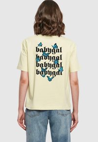 Gul bomulls T-skjorte med svart tekstdesign med "babygal" og blå sommerfugl grafikk på baksiden. Korte ermer, avslappet passform.