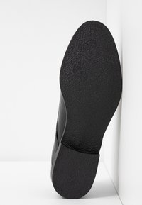 Semelle de chaussure noire avec une surface en caoutchouc texturé, dotée d'un bout arrondi et d'un bord légèrement incliné. Marquée de la taille "39" au dos.