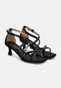 Schwarze Wildleder-High-Heelsandalen mit quadratischer Zehenform und überkreuzten Lackriemen. Kleiner Blockabsatz. Verfügt über einen Schnallenverschluss.