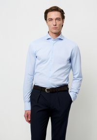 Lichtblauw overhemd met lange mouwen, een kraag en knoopsluiting, gecombineerd met donkerblauwe broek en een bruine riem. Glad oppervlak, aansluitend model.