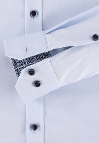 Lichtblauw overhemdd met donkerblauwe knopen, contrasterende geweven manchetten en een gladde textuur. Heeft een klassieke kraag en dubbele manchetten.