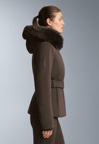 Hnedá izolovaná bunda s kapucňou z umelého kožušinového materiálu, so širokým pásom a prispôsobeným strihom. Vyznačuje sa hladkou štruktúrou a minimalistickým dizajnom.