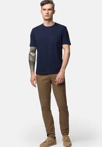 Granatowa koszulka z krótkim rękawem z kieszonką na piersi, w komplecie z brązowymi spodniami i beżowymi butami. Materiał wydaje się gładki i lekki.