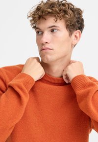 Oransje strikkegenser med ribbet rund hals og lange ermer, laget av et mykt og strukturert stoff.