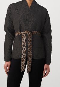 Quiltad svart jacka med omslagsdesign, försedda med ett leopardmönstrat bälte. Inkluderar två framfickor och en bekväm passform.