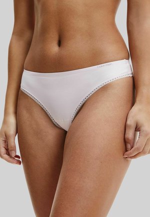 Woman wearing light pink Calvin Klein bikini-style underwear with lace trim, shown from midriff to upper thighs against a plain background.
