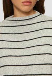 Lichtgrijze trui met horizontale zwarte strepen, hoge halslijn en een zachte, gestructureerde stof. Geen zichtbare sluitingen of versieringen.
