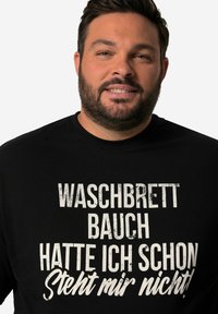 Černé tričko s velkým bílým textem "WASCHBRETT BAUCH HATTE ICH SCHON STEHT MIR NICHT!" Vyrobené z bavlny s designem s kulatým výstřihem.