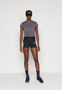 Lilla lühikeste varrukatega sportlik topp halli logoga, kombineeritud mustade lühikeste pükstega, millel on valged küljetriibud ja mustad spordijalatsid.