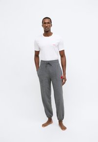 Άσπρο T-shirt με στρογγυλή λαιμόκοψη και κόκκινο λογότυπο "HUGO", σε συνδυασμό με γκρι στενά φαρδιά φόρμας με ελαστική μέση και κόκκινη ετικέτα λεπτομέρειας.