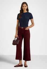 Sötétkék, testhez simuló rövid ujjú felső, bordó, magas derekú, széles szárú nadrág, arany színű övcsat, kis bordó kézitáska és hozzáillő balerina cipők.