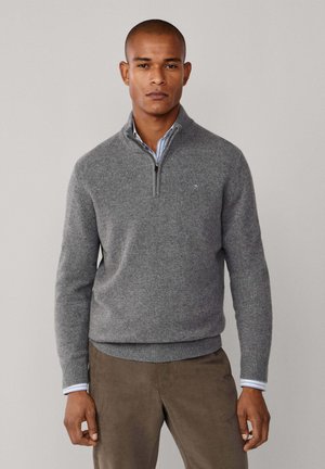 Grauer Strickpullover mit einem Reißverschlusskragen, gerippten Bündchen und Saum. Über einem blau-weiß gestreiften Hemd getragen. Glatte Textur, lässiges Design.