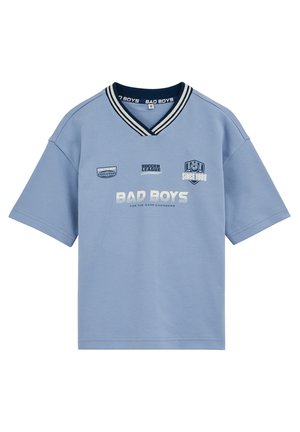 Camiseta de manga corta azul claro con cuello en V a rayas marinas, texto "BAD BOYS", logotipos temáticos de fútbol y emblema "Since 1988" en el frente.