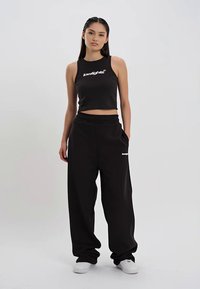 Svart cropped tanktop med hvit logo og matchende løstsittende joggebukser. Begge plaggene er laget av myk stoff og har et avslappet design.