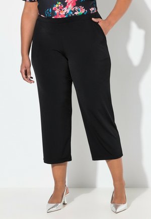 Pantaloni cropped neri con una texture liscia, dotati di tasche laterali e una cintura elastica. Abbinati a scarpe con tacco alto argentate metalliche.