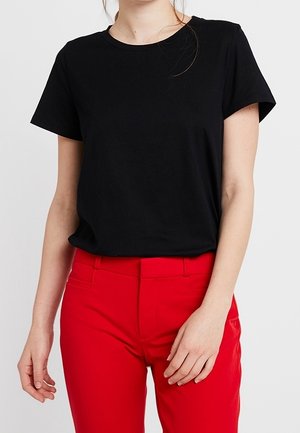 T-shirt en coton noir à manches courtes, col rond, associé à un pantalon rouge taille haute, présentant une texture lisse et une coupe ajustée.