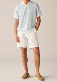 Vaaleansininen kuvioitu poolopaita, jossa valkoinen kaulus, yhdistettynä valkoisiin shortseihin ja ruskeisiin purjehduskengännäköisiin kenkiin. Painotus hengittävään kangaslaatuun ja rentoon muotoiluun.