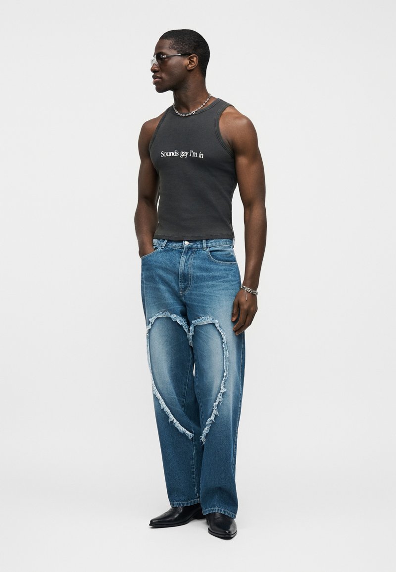 Čierne tielko s bielym nápisom, kombinované so svetlomodrými roztrhanými džínsami s prierazmi v tvare srdca. Čierne topánky dopĺňajú outfit.