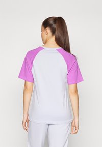 Kortärmad t-shirt med lila raglan-design, vit kropp, tillverkad av mjukt tyg, med rundad halsringning och avslappnad passform.