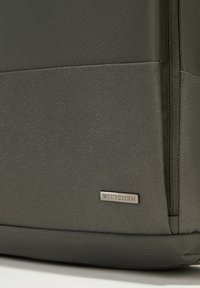 Donkergrijze, gestructureerde rugzak met een glad paneel en een rits, voorzien van een metalen "WITTCHEN" label op de voorkant onderaan.